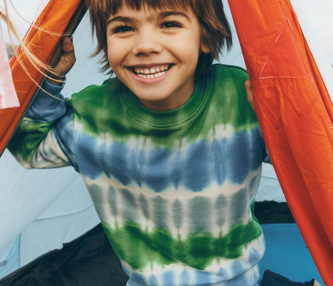 Child wearing a tie-dye shirt with green, blue, and white colors, standing outdoors.