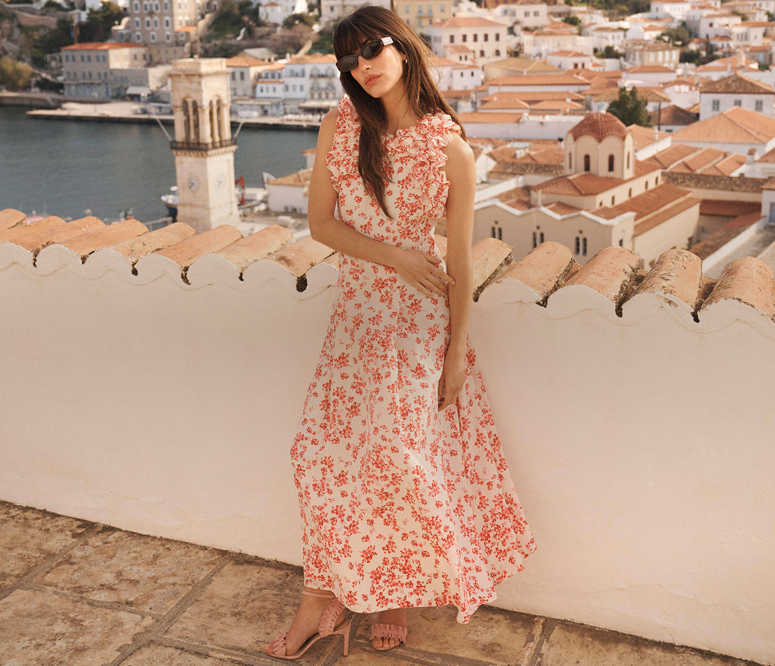 Woman in a floral dress standing on a rooftop with a scenic view of a town.