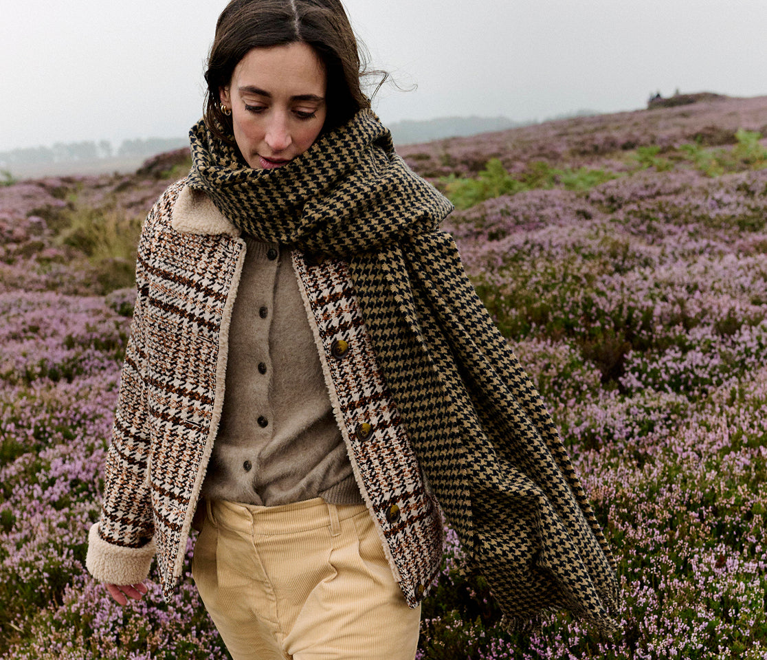 Woman wearing a patterned coat and scarf in a field of purple flowers