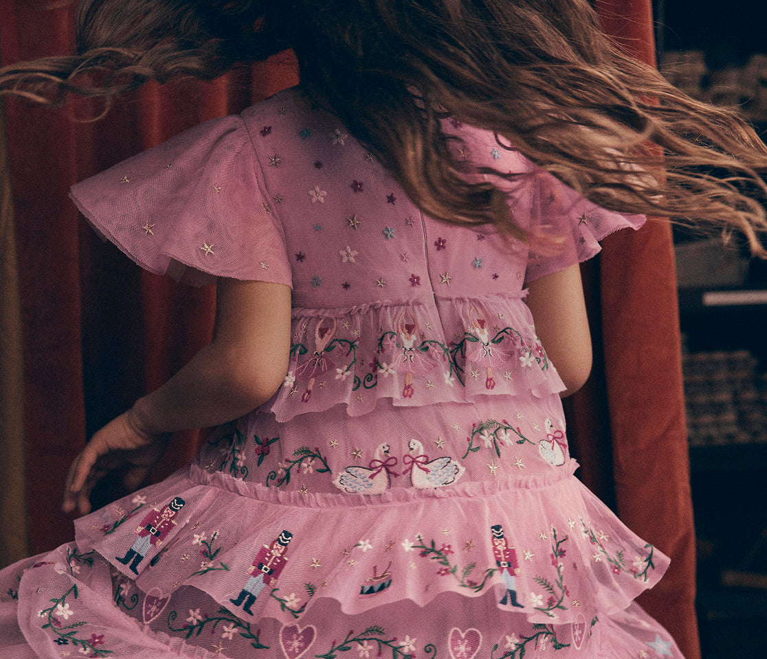 Child wearing a pink tulle dress with embroidered swans, nutcracker figures, floral details and tiered ruffles