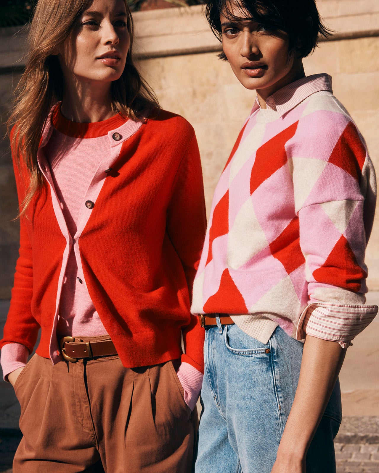 Two women wearing colorful sweaters and pants standing outdoors.
