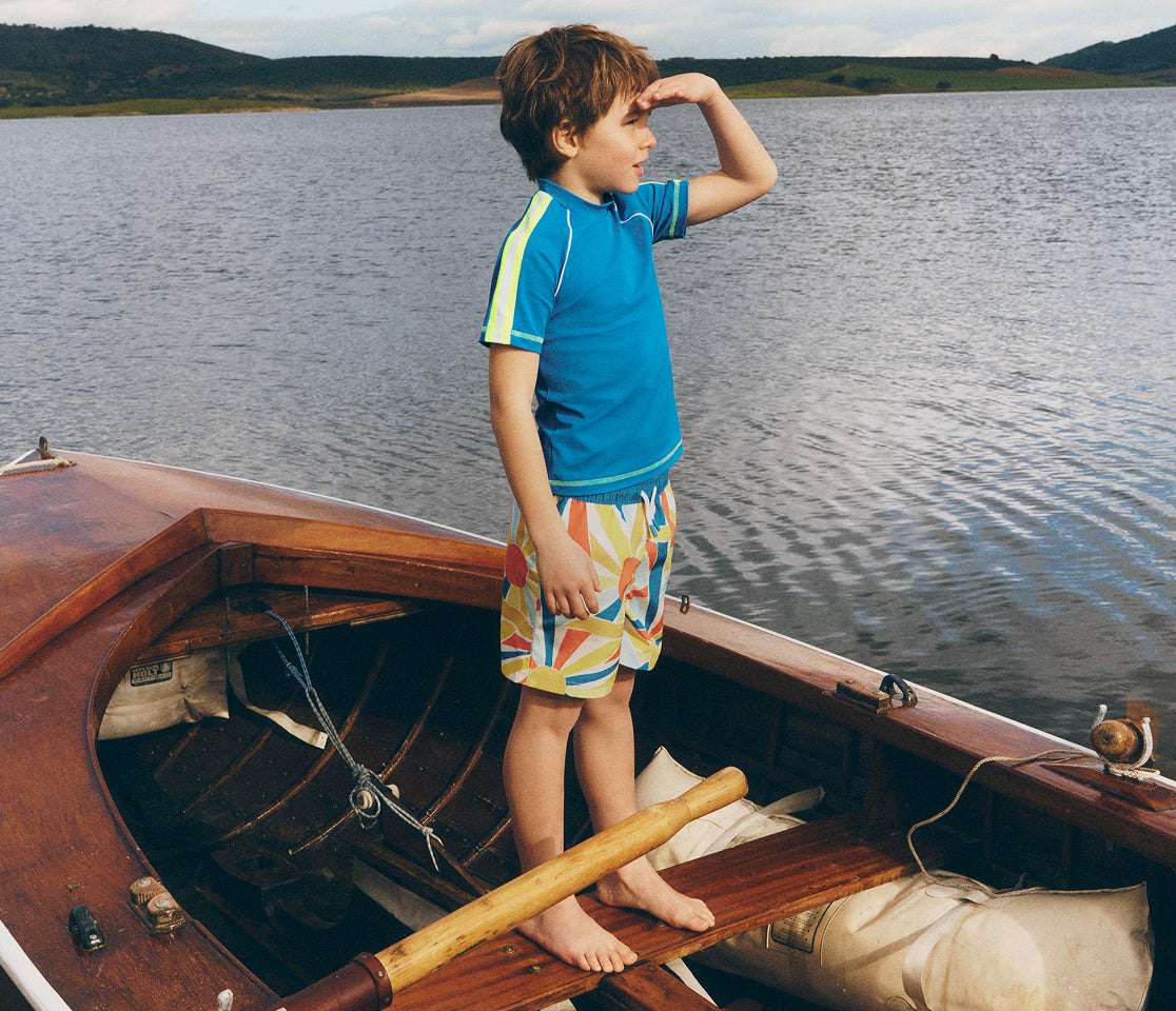 Child standing on a wooden boat by a lake