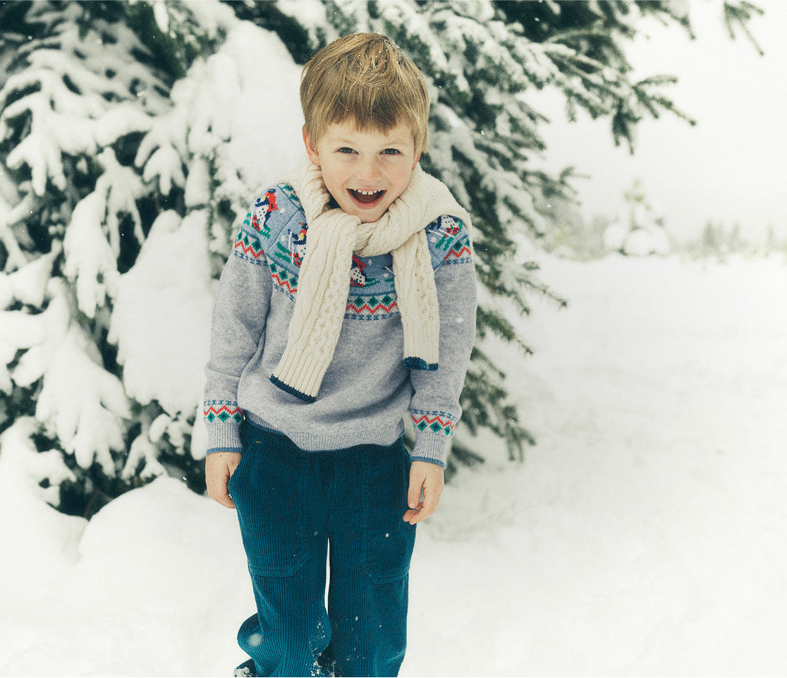 Child wearing a patterned sweater and scarf standing in a snowy forest