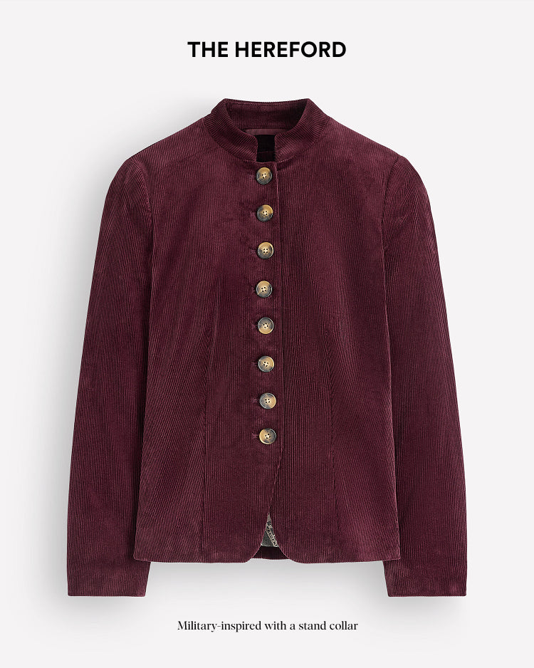 A military-inspired corduroy jacket in deep burgundy with a stand collar and decorative gold buttons, shown against a light gray background with text overlays reading 'THE HEREFORD' at the top and 'Military-inspired with a stand collar' at the bottom.
