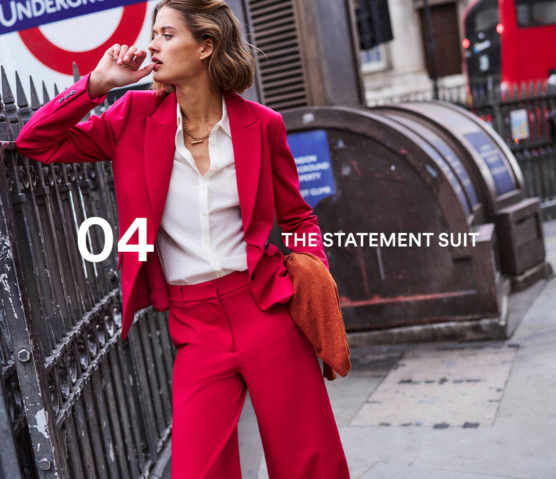 Woman in a red suit standing in an urban setting with a London Underground sign in the background.