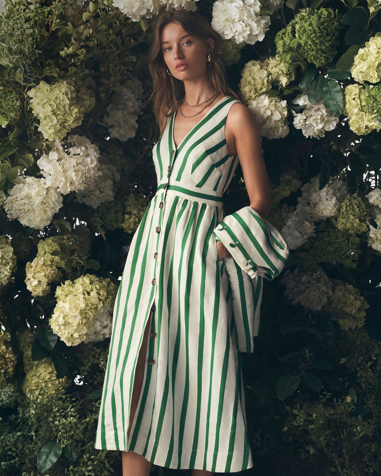 Woman in a green and white striped dress standing against a floral wall.