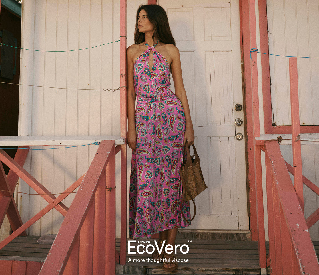 Woman in a pink patterned dress standing in front of a white door with 'EcoVero' branding.
