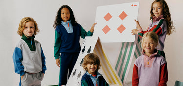 Five children in colorful clothing standing around a large playing card with geometric shapes on a plain background.