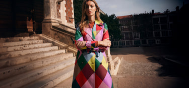 Woman in a colorful coat standing on steps with buildings in the background