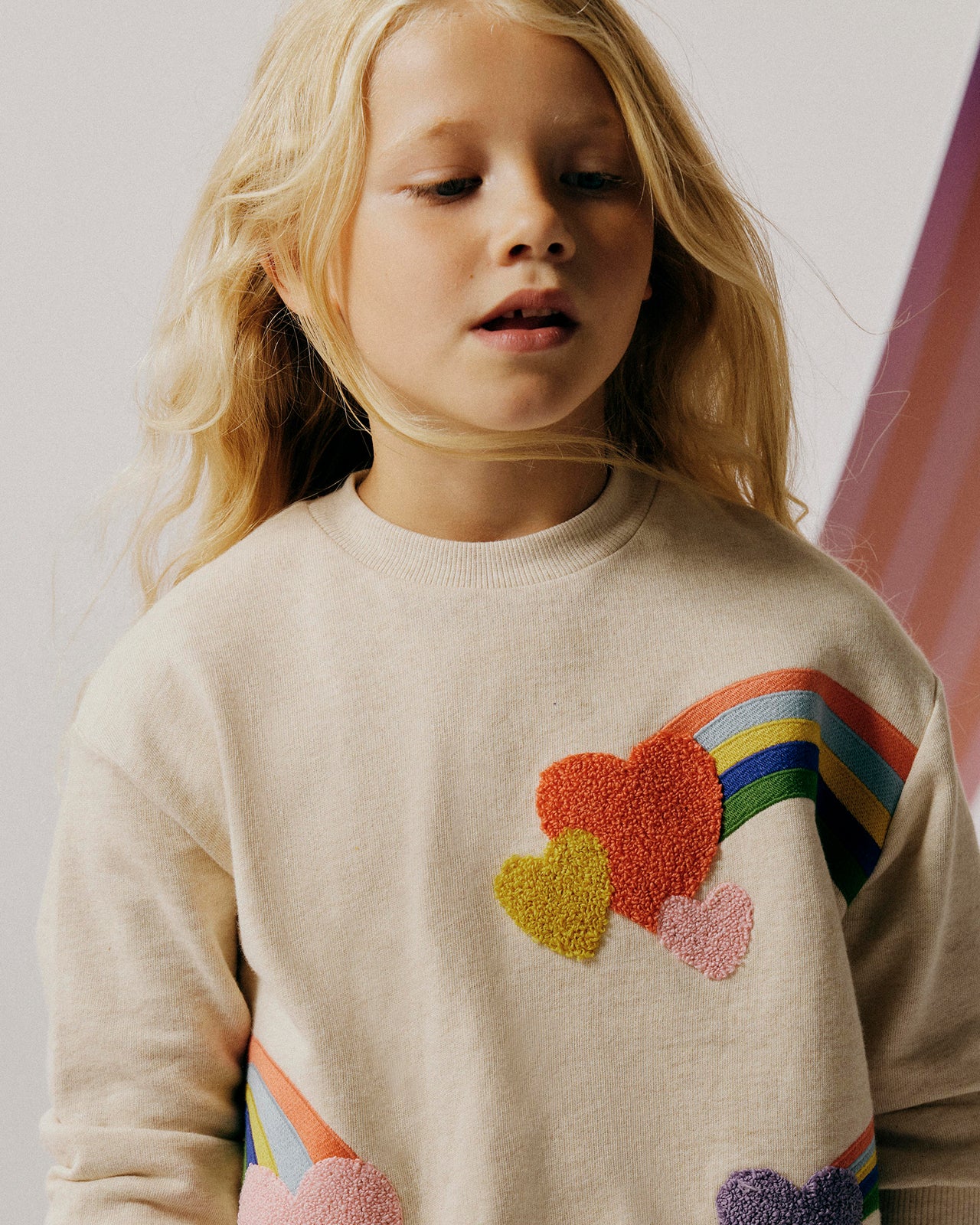 Child wearing a sweater with colorful heart and rainbow designs.