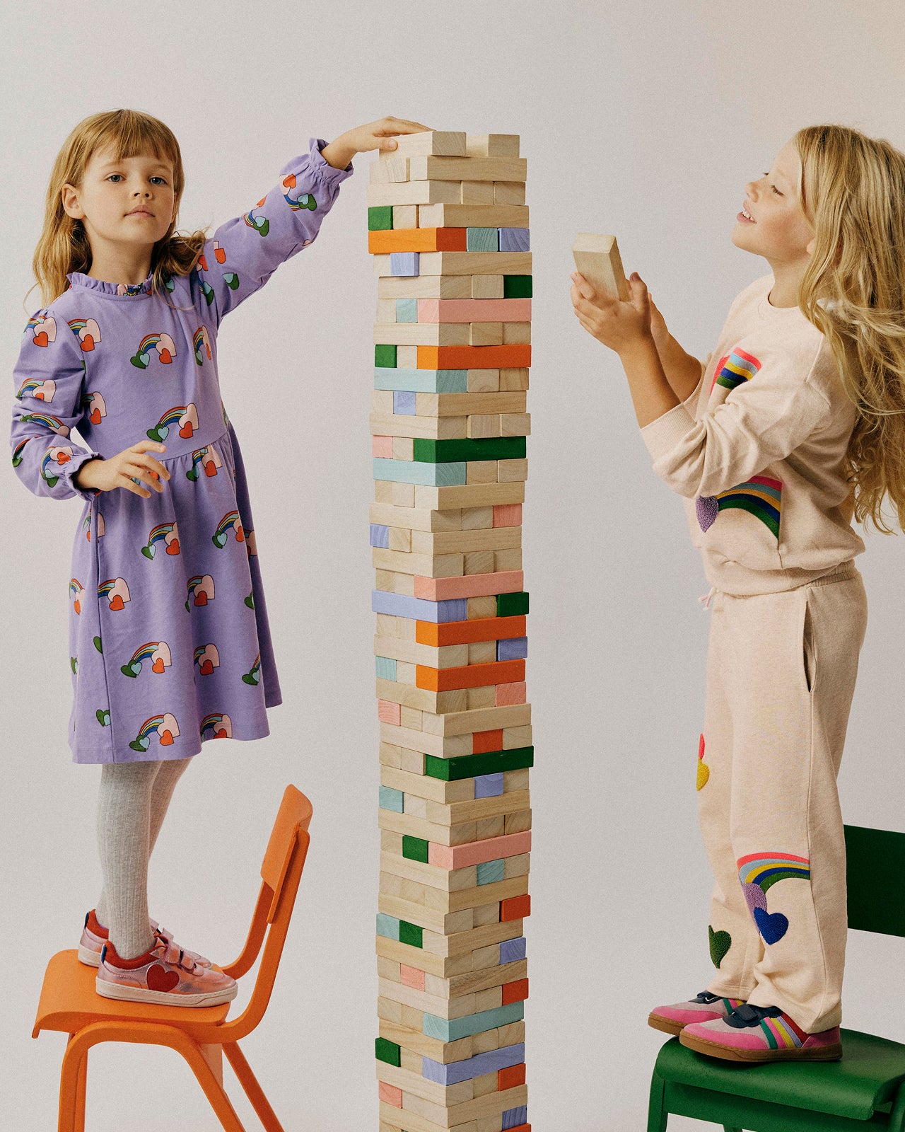 Two children playing with a tall tower of colorful wooden blocks.
