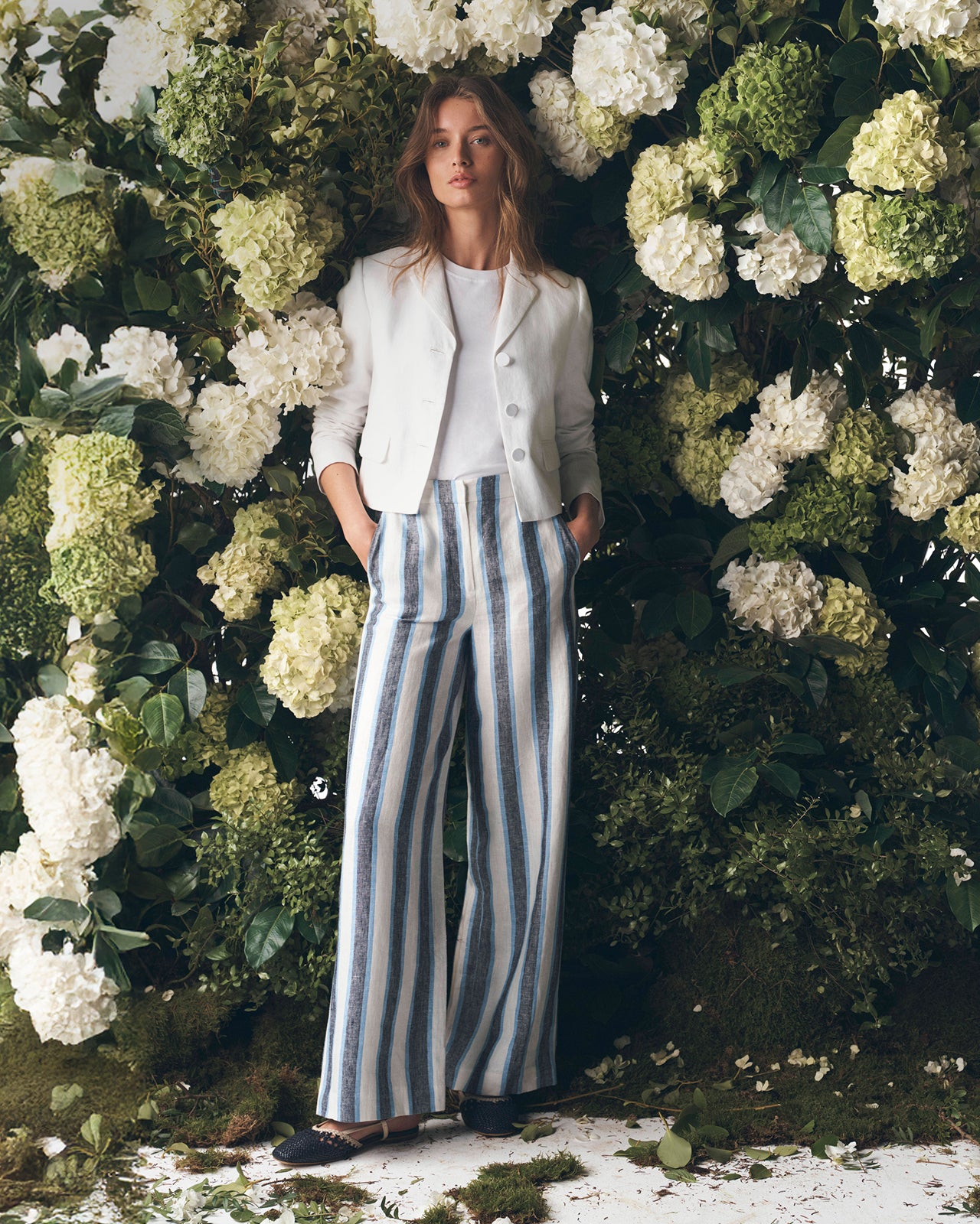 Woman standing in front of a floral wall with white and green flowers.