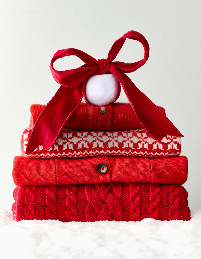 Stack of red sweaters with a decorative bow on a white background