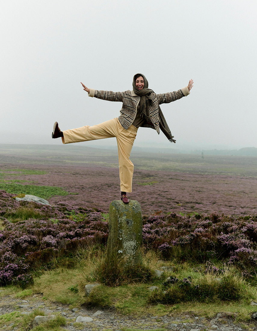 Person balancing on a rock in a vast, open landscape with purple heather.