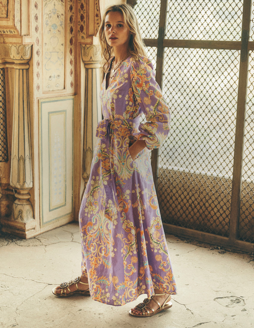 Woman wearing a long, patterned dress standing in a room with decorative elements.
