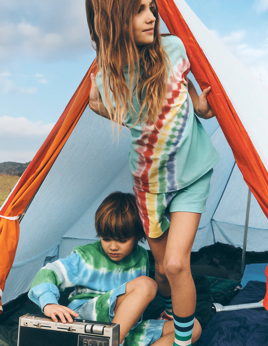 Two children in tie-dye clothing inside a tent with a clear sky background