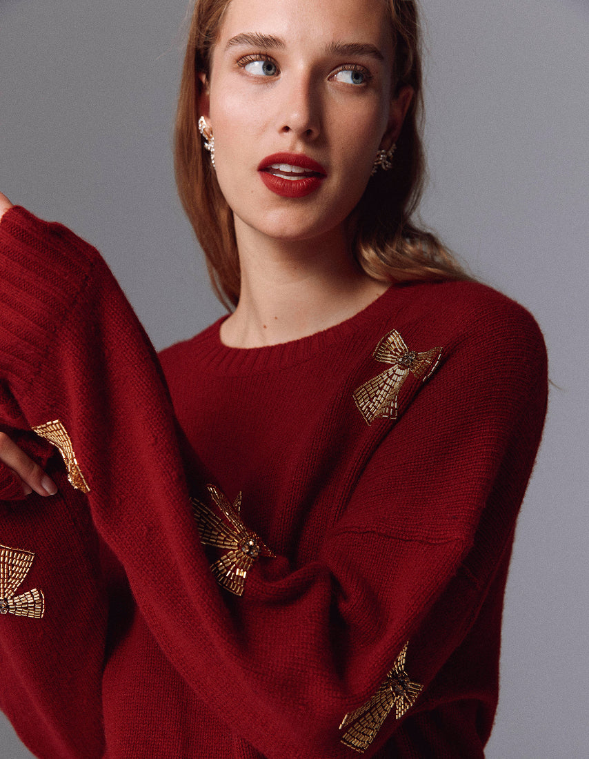 Woman wearing a red sweater with gold butterfly patterns against a gray background