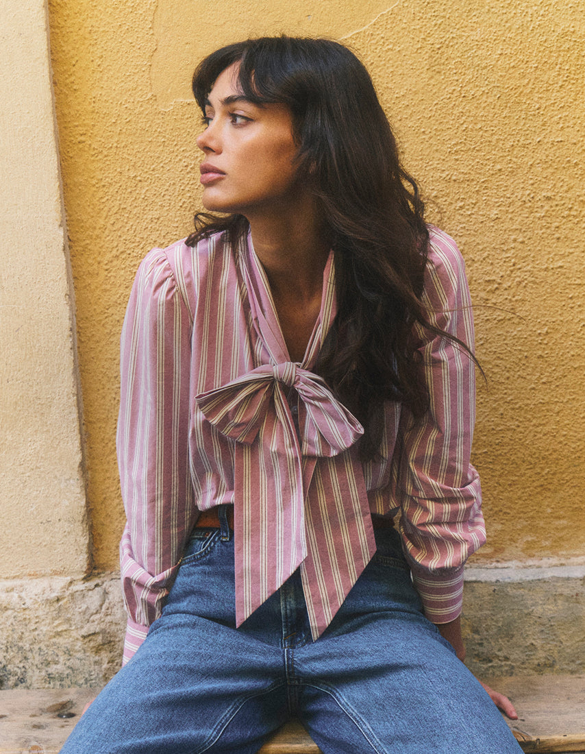 Woman wearing a striped shirt with a bow tie against a yellow wall.