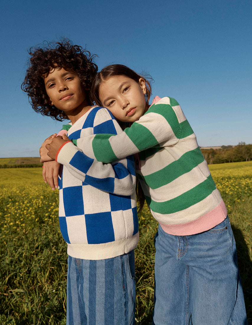 Two children wearing colorful sweaters standing in a field with a clear blue sky.
