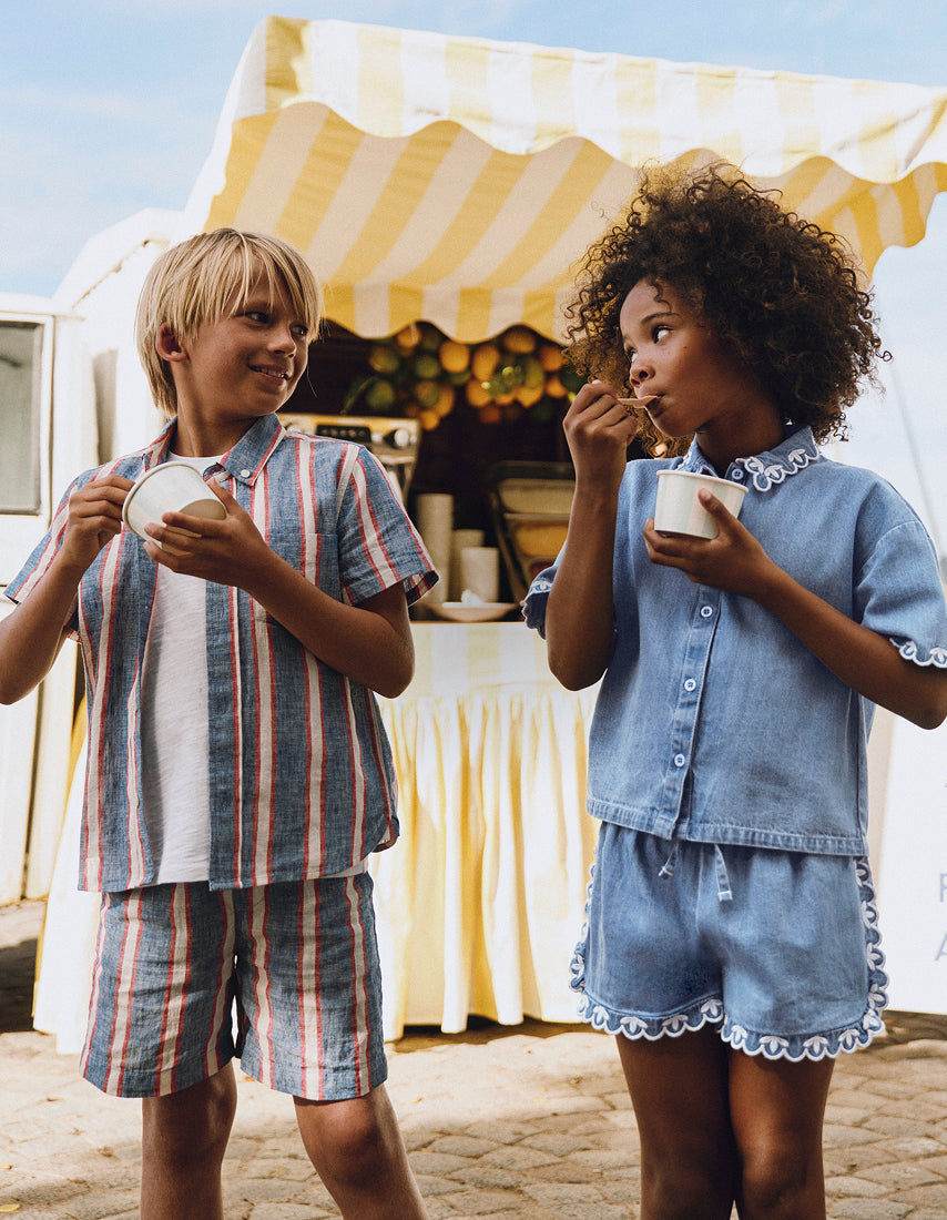 Two children in matching outfits standing under a striped canopy.