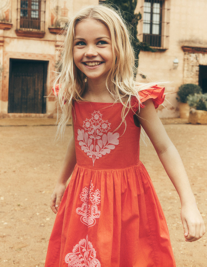 Young girl in a red dress with floral patterns standing outdoors.