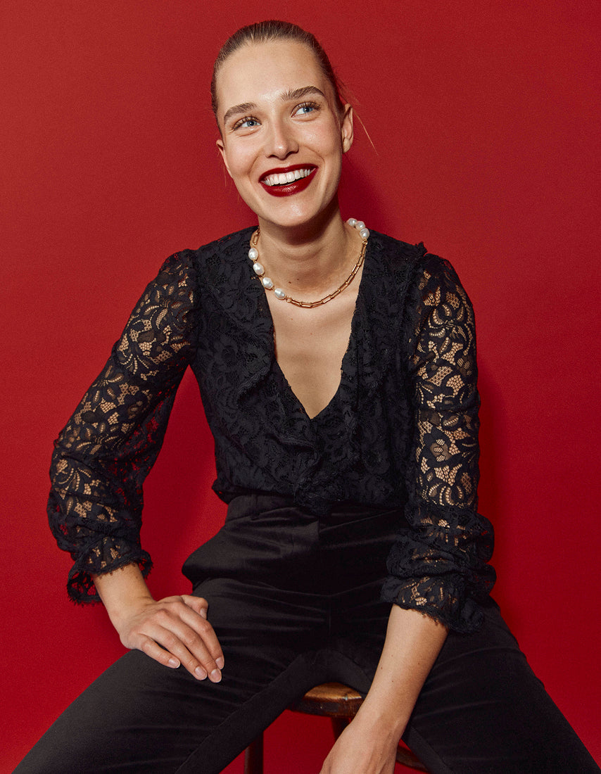 Woman wearing a black lace top and black pants against a red background