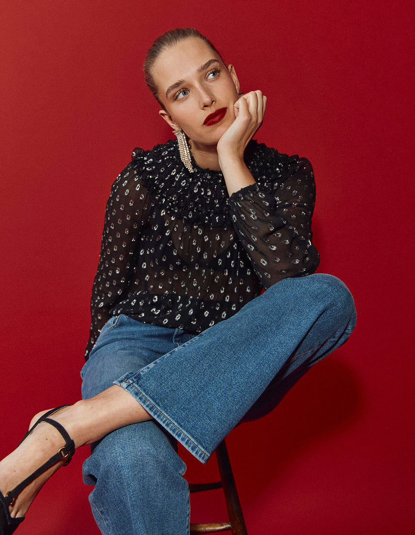 A woman sitting on a stool wearing a black polka dot top