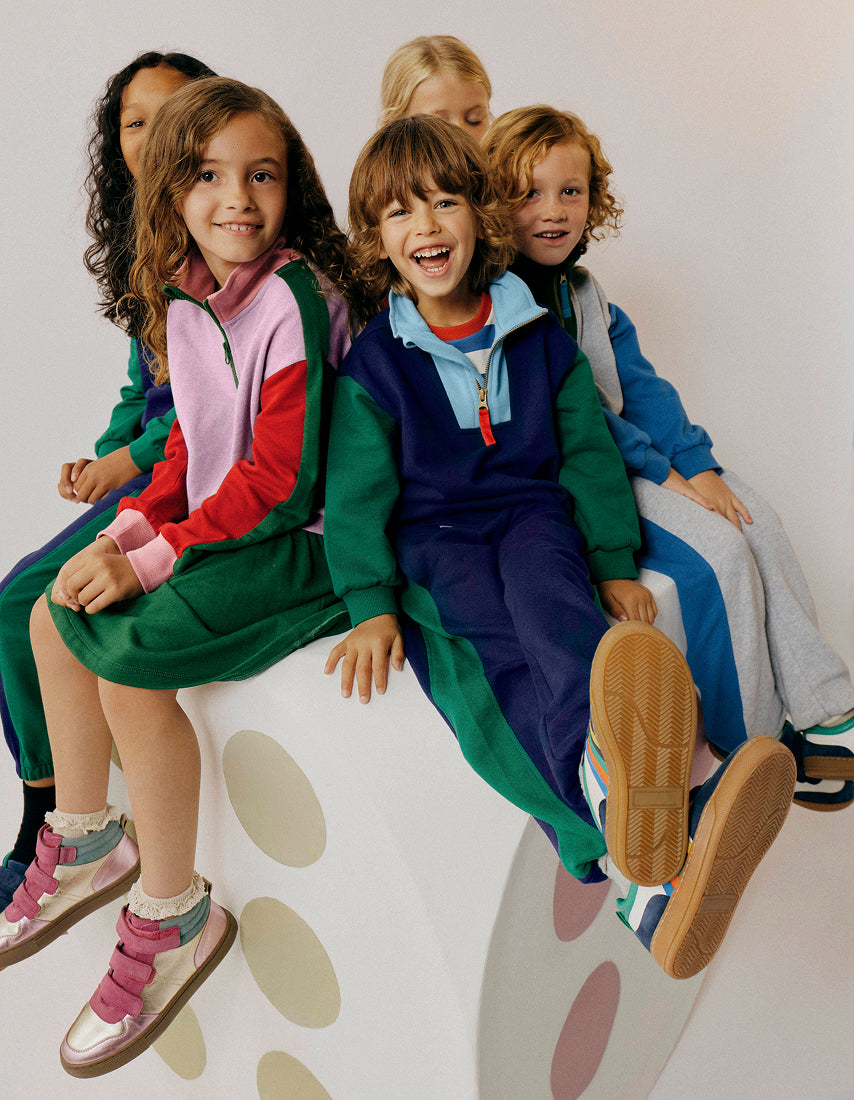Children sitting on a polka dot chair wearing colorful outfits.
