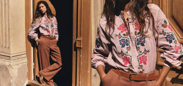 A model wears a light pink long-sleeve button-up shirt with colorful floral embroidery on the front and sleeves, paired with brown wide-leg trousers and a brown belt, shown in a split-screen lifestyle shot against a warm-toned stone and wood doorway.