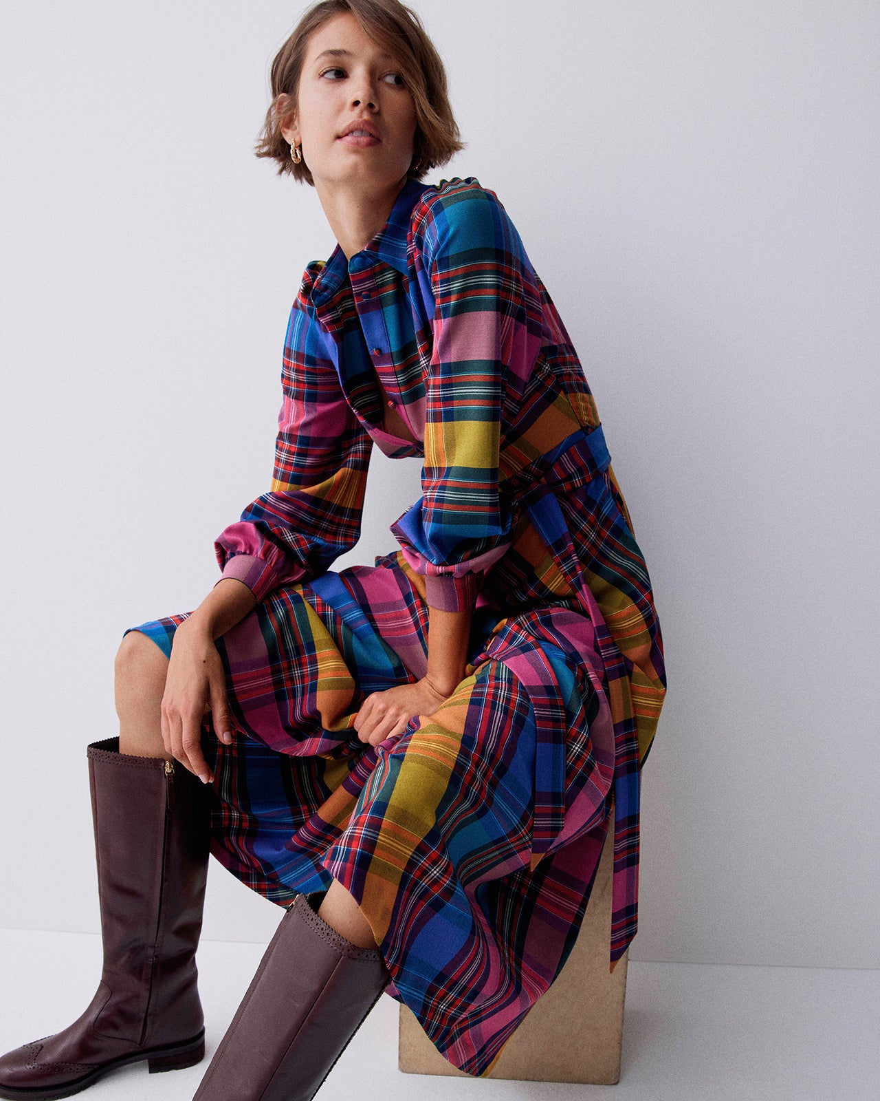 Woman wearing a colorful plaid dress sitting on a white background