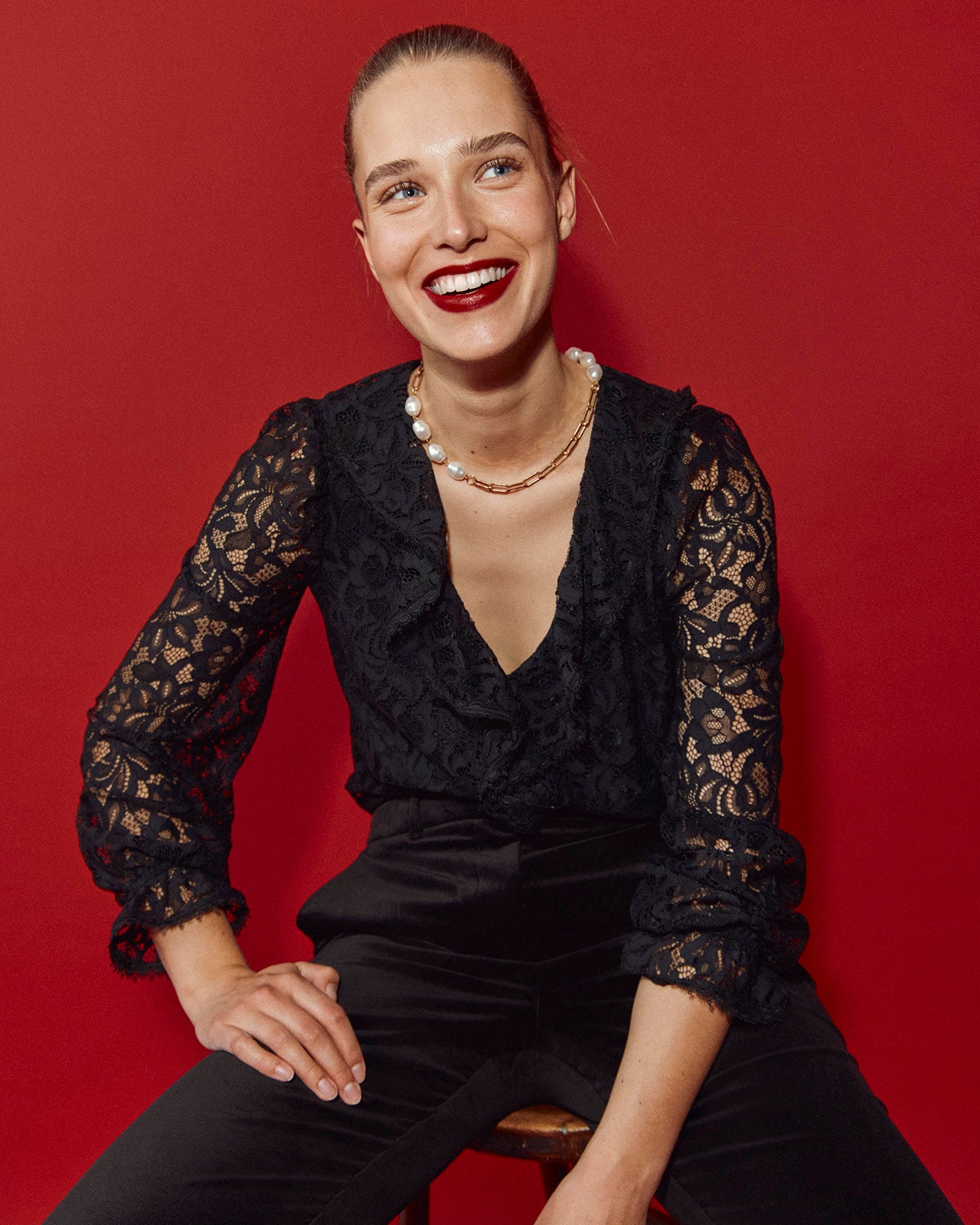 A women wearing a black top sitting down against a red background