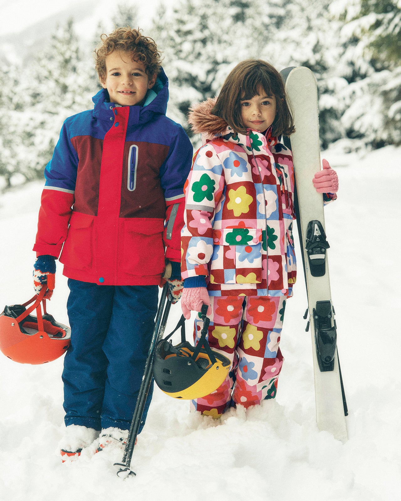 Two children in colorful winter outfits with skis and ski equipment in a snowy setting.