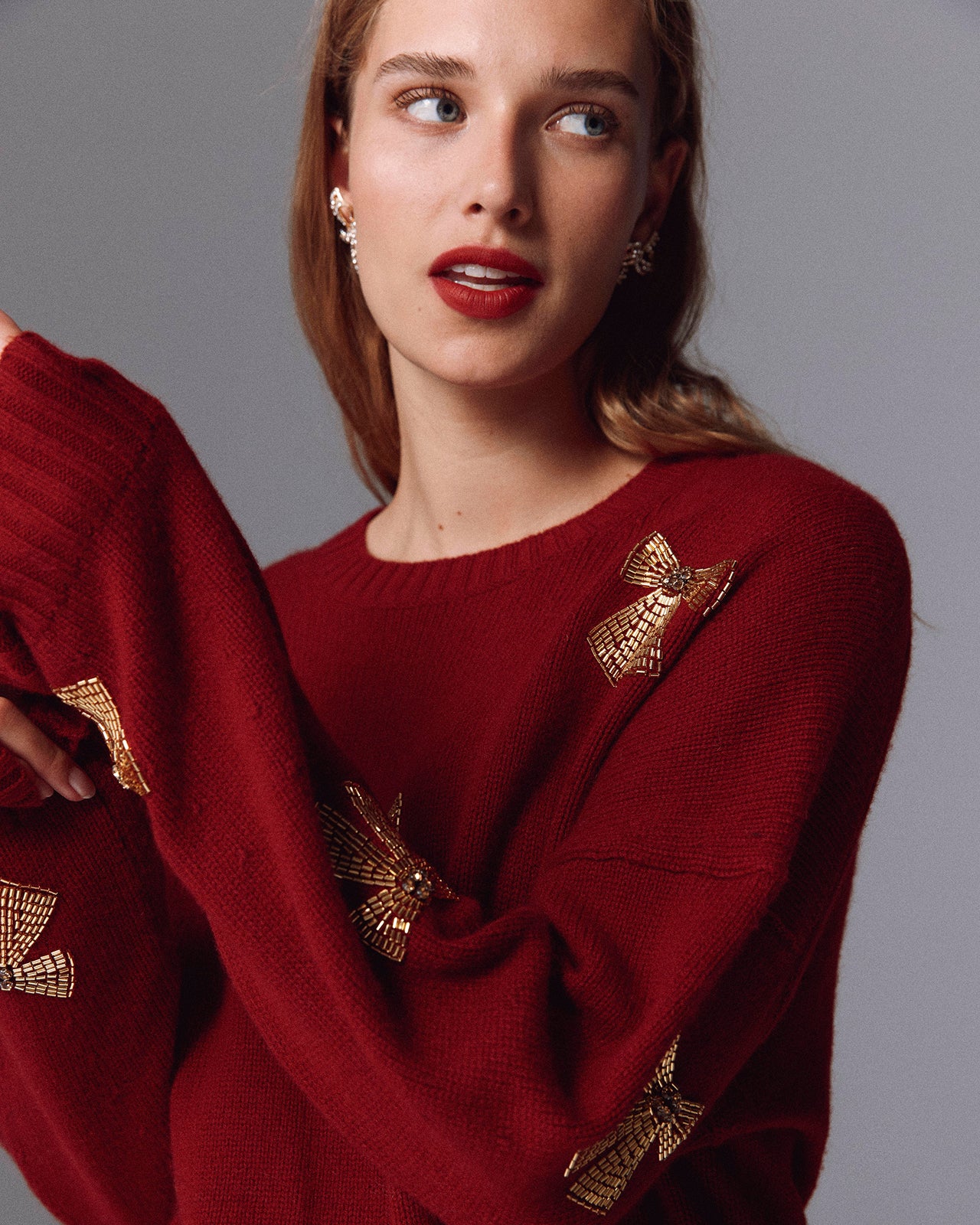 Woman wearing a red sweater with gold butterfly designs on a gray background
