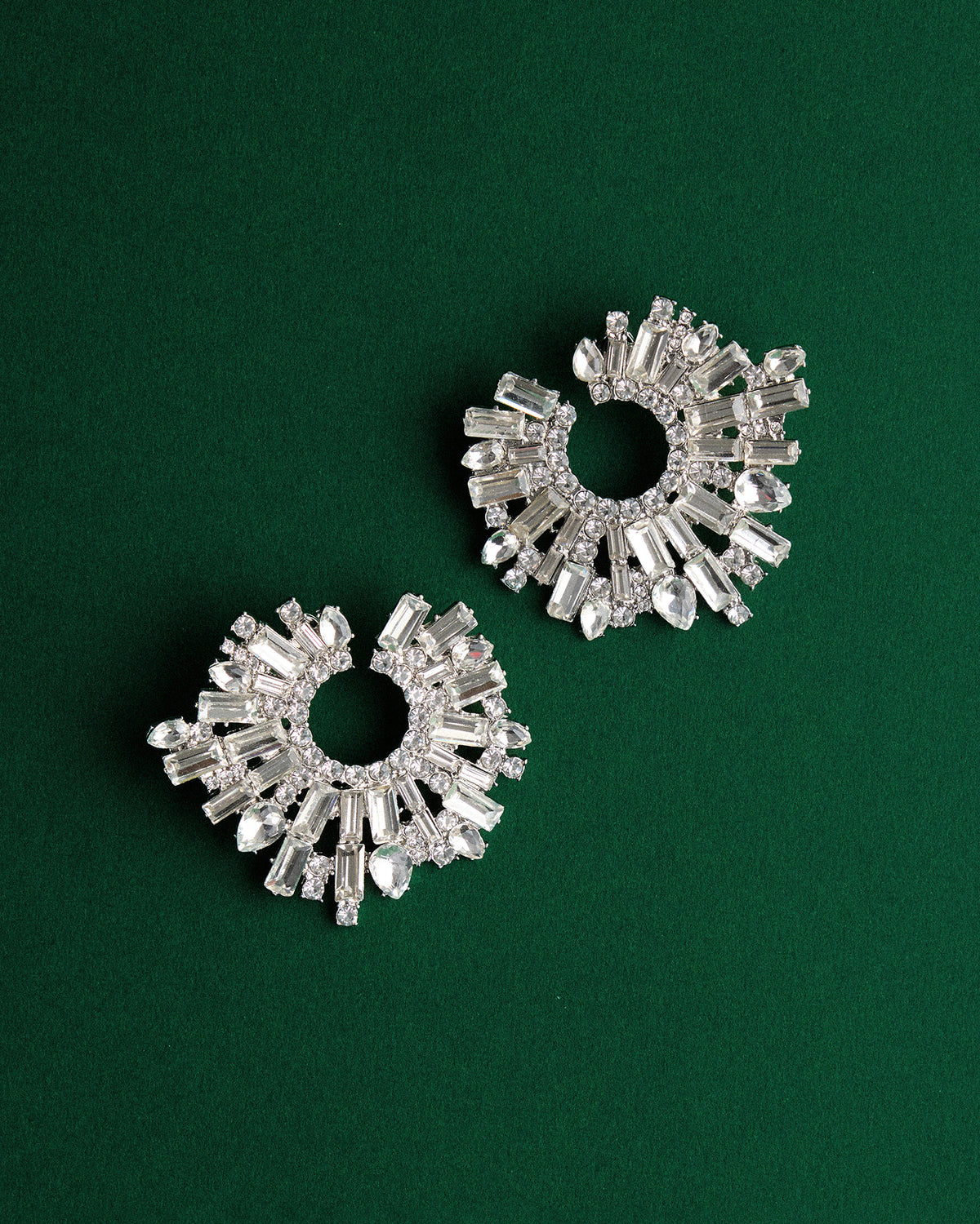 Pair of silver crystal statement earrings with circular design on a green background