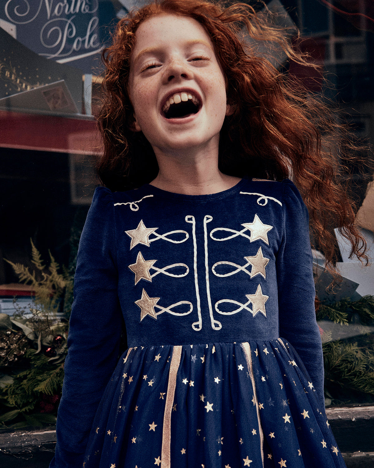 Girl with long red hair wearing a navy velvet dress with gold embroidered stars and decorative detailing, finished with a star-print tulle skirt.