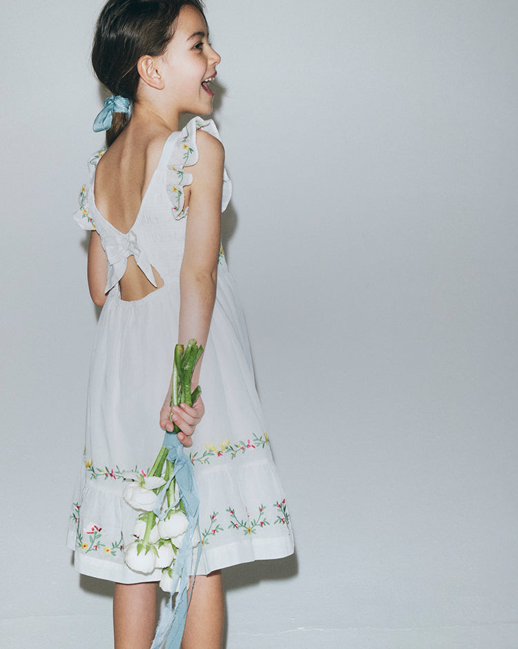 Woman wearing a white dress with floral embroidery on a plain background