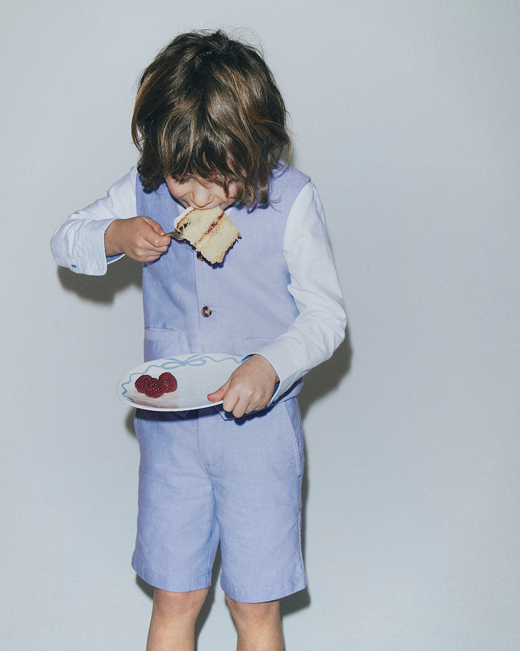 Child in a light blue outfit eating from a plate with a white background