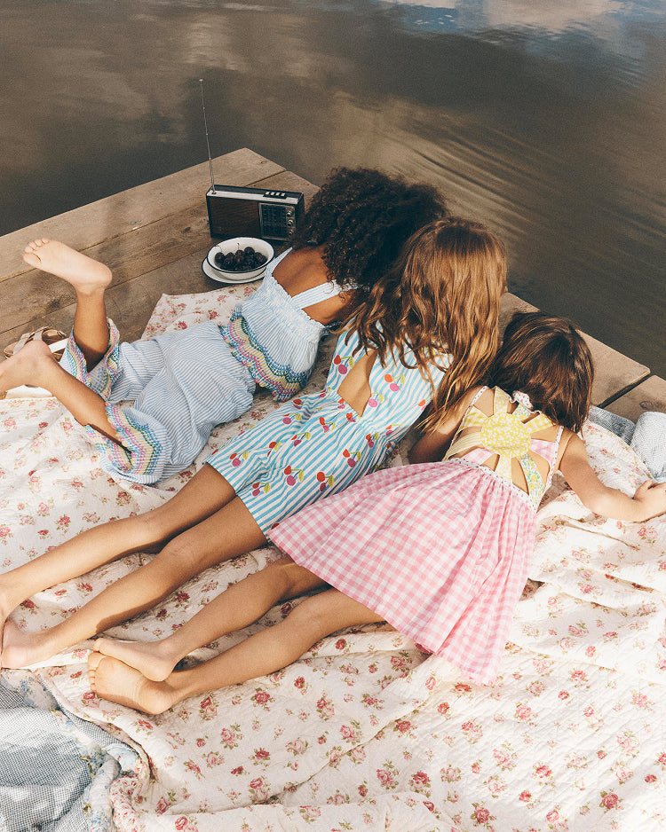 Three children in pajamas lying on a bed with a floral blanket, looking at a radio.