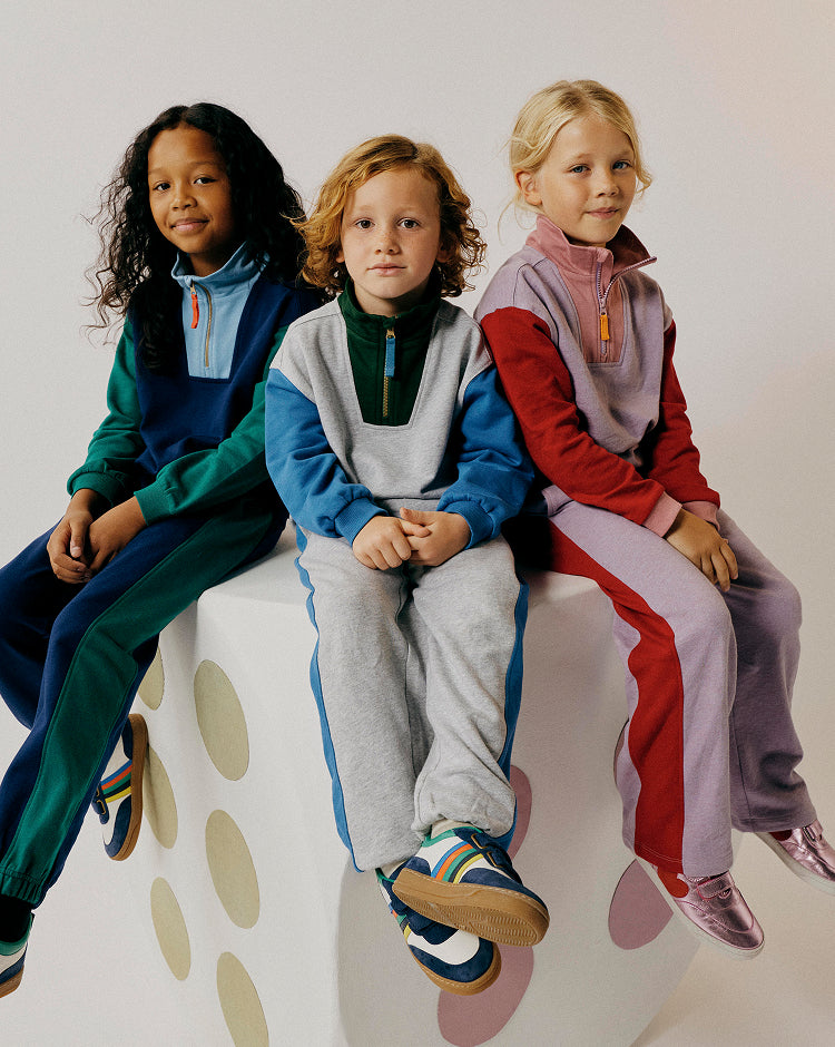 Three children sitting on a polka dot chair wearing colorful outfits.