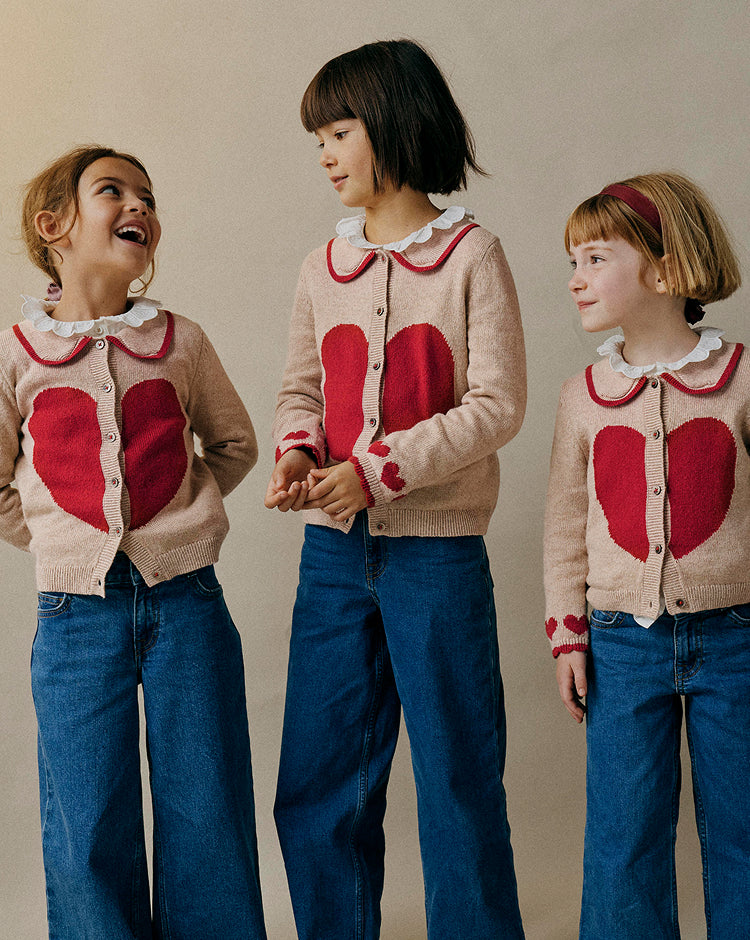 Three children wearing matching cardigans with red heart designs on a beige background