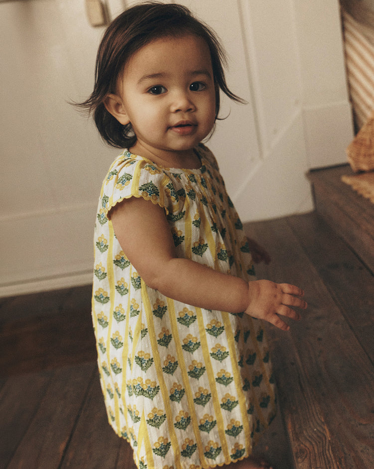Child wearing a yellow dress with a floral pattern indoors.