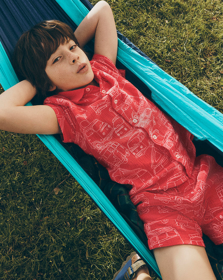 Child in a red outfit with white patterns lying on a blue hammock in a grassy area