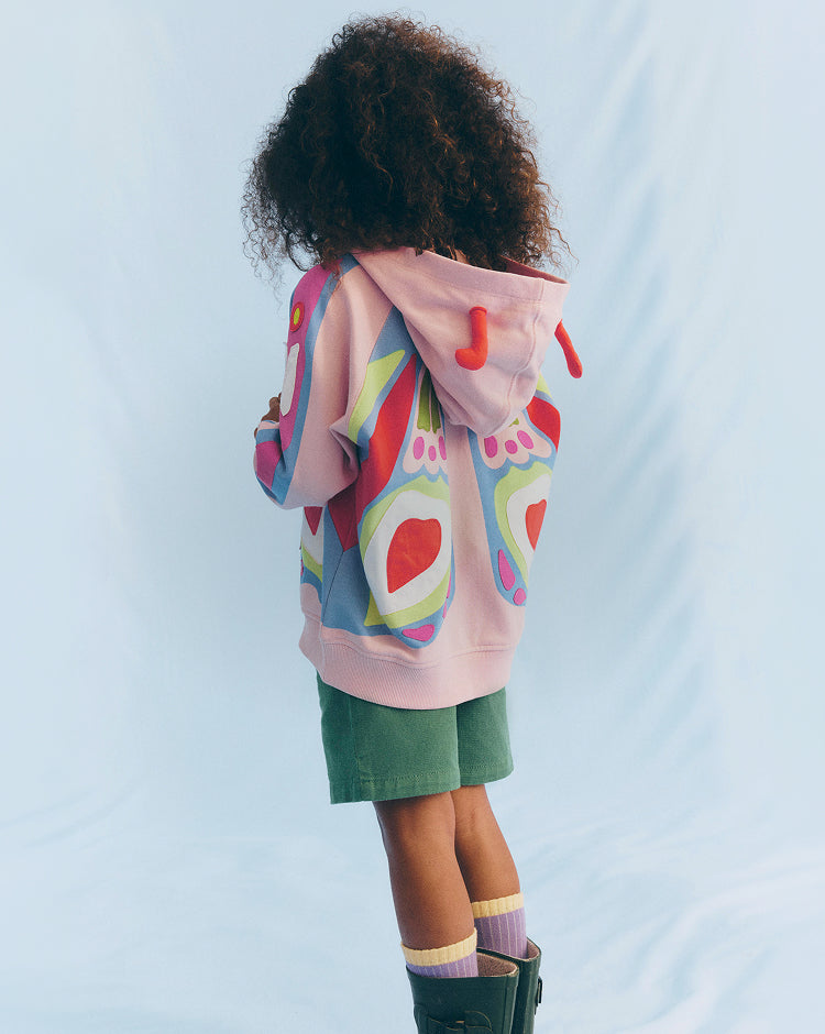 Child wearing a colorful hoodie with pink duffle bag on a light blue background
