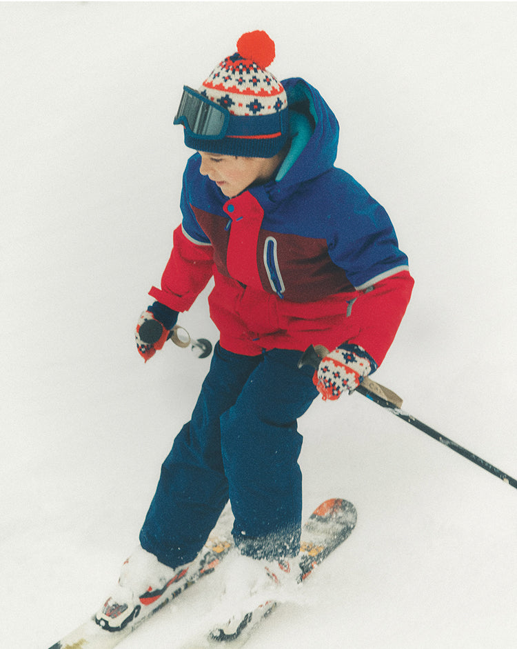 Child skiing on a snowy surface wearing a colorful outfit