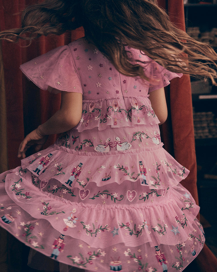 Child wearing a pink tulle dress with embroidered swans, nutcracker figures, floral details and tiered ruffles