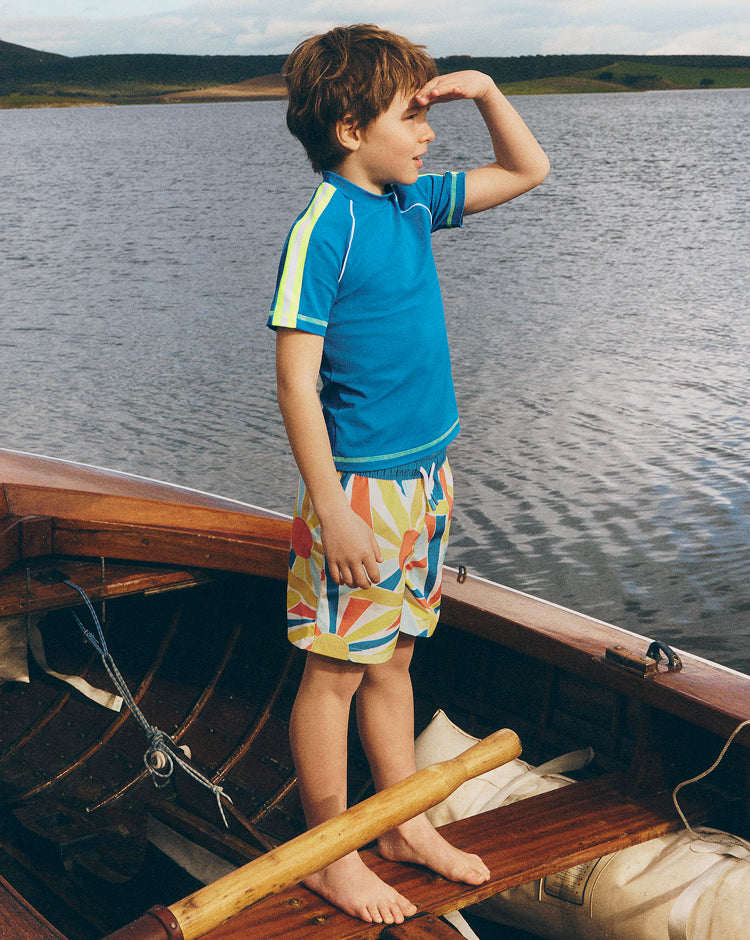 Child standing on a wooden boat by a lake