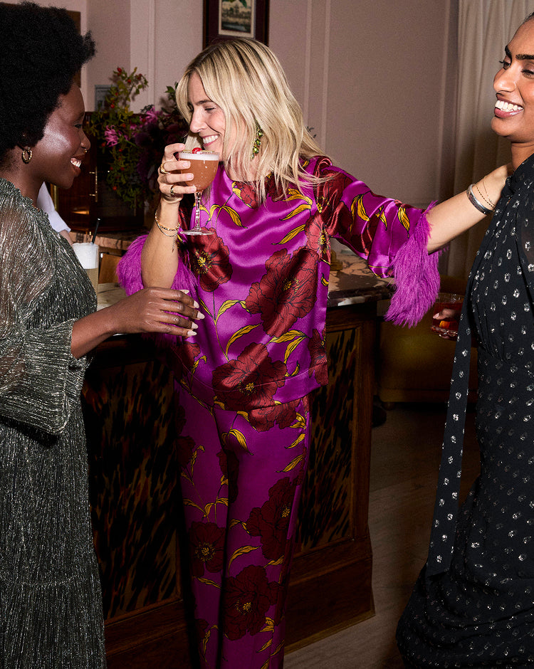 Three women socializing at a party, one in a purple outfit holding a drink.