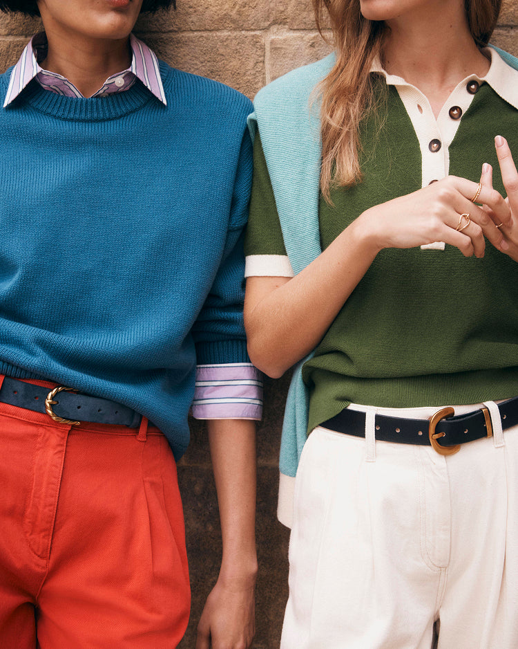 Two people wearing colorful sweaters and pants against a brick wall.