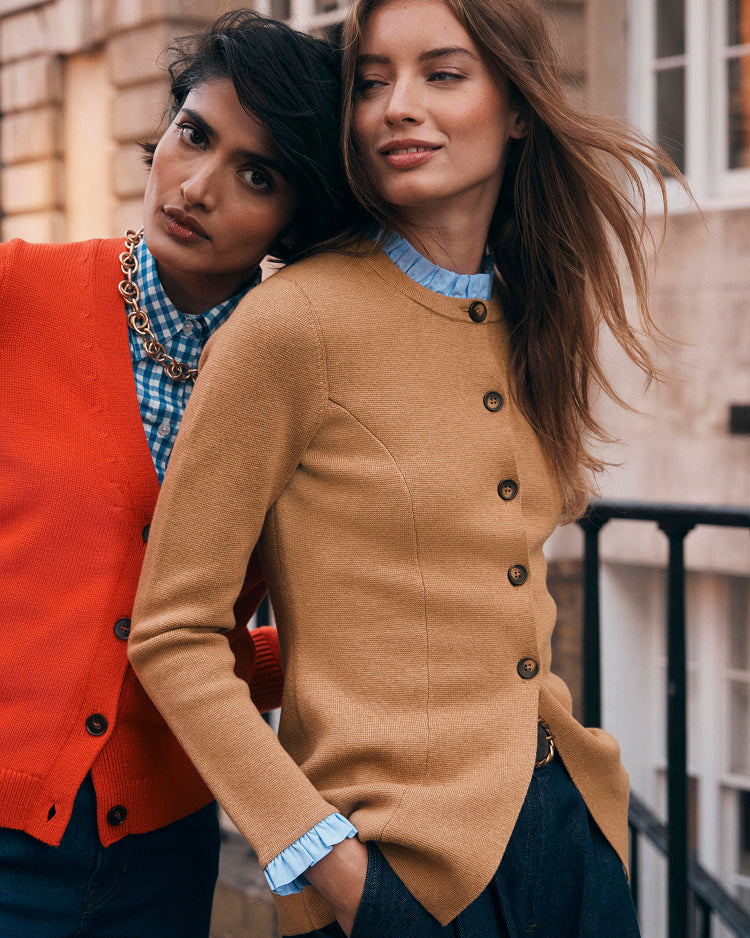 Two women standing close together, one wearing a red cardigan and the other a tan cardigan with buttons.