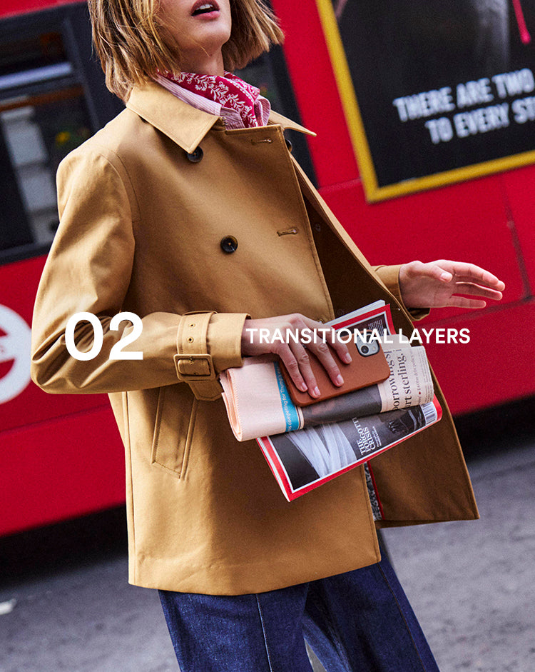Person wearing a tan coat holding books with a red bus in the background